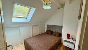 A bedroom with a sloped ceiling, a skylight, a bed with a patterned bedspread, a bedside table with a red cup, and a wall-mounted lamp. - Duplex T3 with parking in Cauterets, near cable cars (Cauterets)