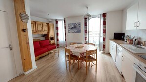 A cozy living area with a red sofa, wooden cabinets, a dining table with chairs, and a kitchen area with white cabinets and a sink.