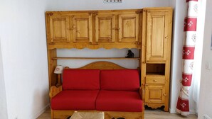 A small, cozy room with a wooden bed, a red sofa, and a wooden cabinet with shelves.