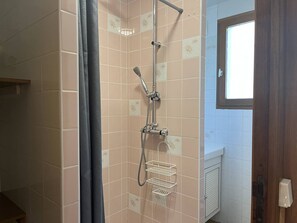 Een douche met een handdouche en een wandmengkraan, een handdoekrek en een raam met uitzicht.