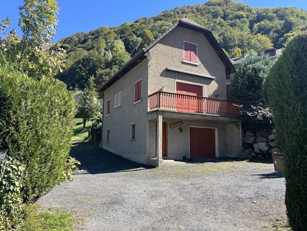A two-story house with a balcony, a garage, and a gravel driveway.