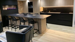 A modern kitchen with a central island, black bar stools, and a built-in oven.