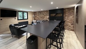A modern kitchen with a long dining table, black chairs, a TV, and a stone wall backsplash.