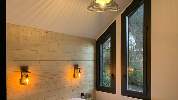 A bedroom with a wooden headboard, two bedside lamps, a large bed, and a window with a view of trees.