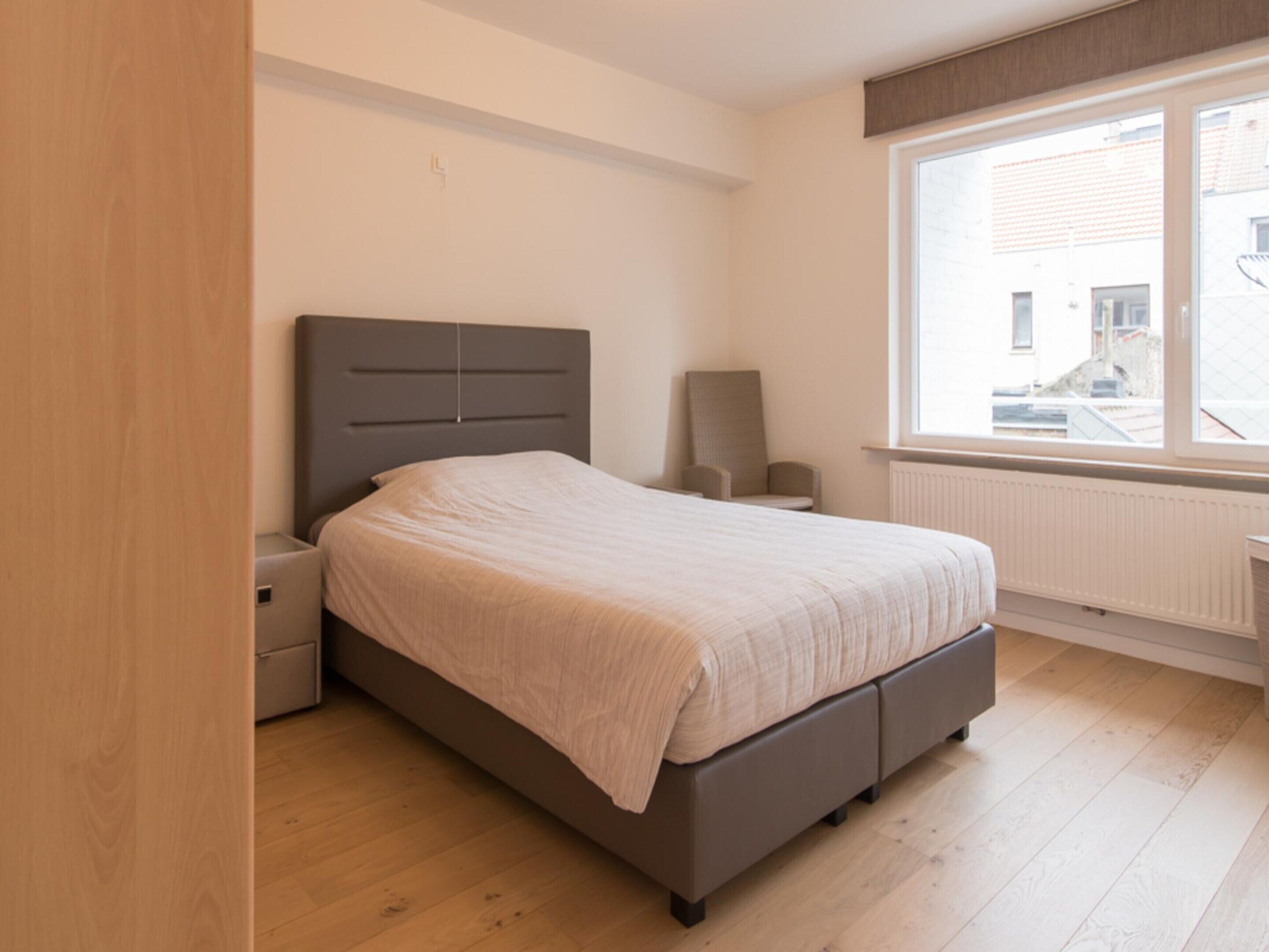 A bedroom with a bed, nightstands, a chair, and a window.