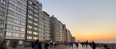 Un paseo marítimo con edificios modernos, cielo despejado y gente caminando.