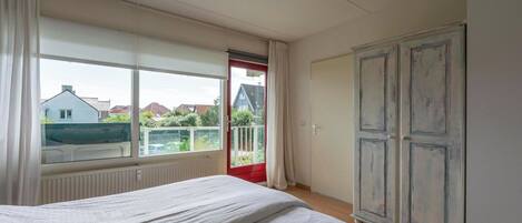 A bedroom with a large bed, a wardrobe, and a window with a view of the outside.