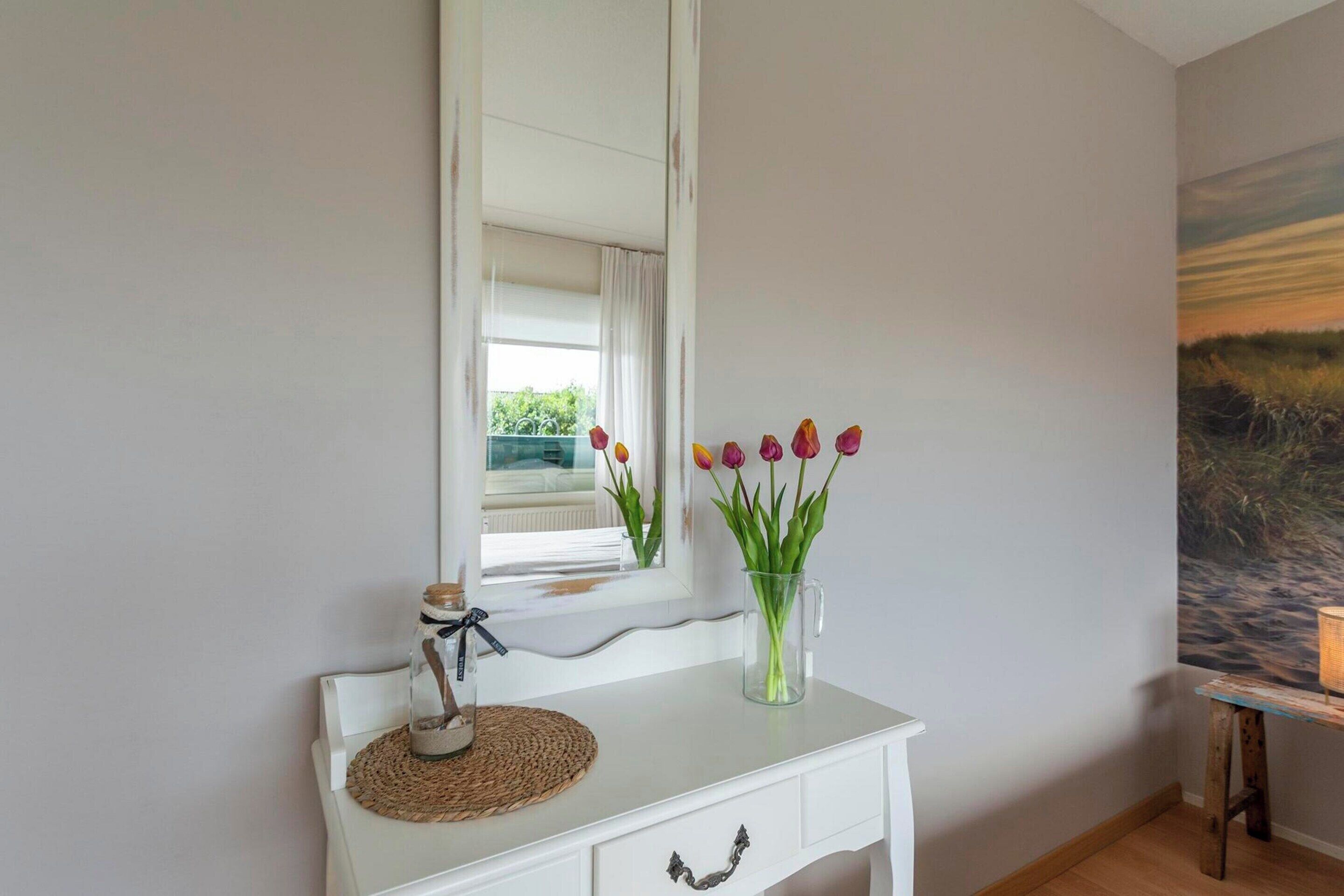 A white console table with a vase of tulips, a small jar, and a woven placemat.