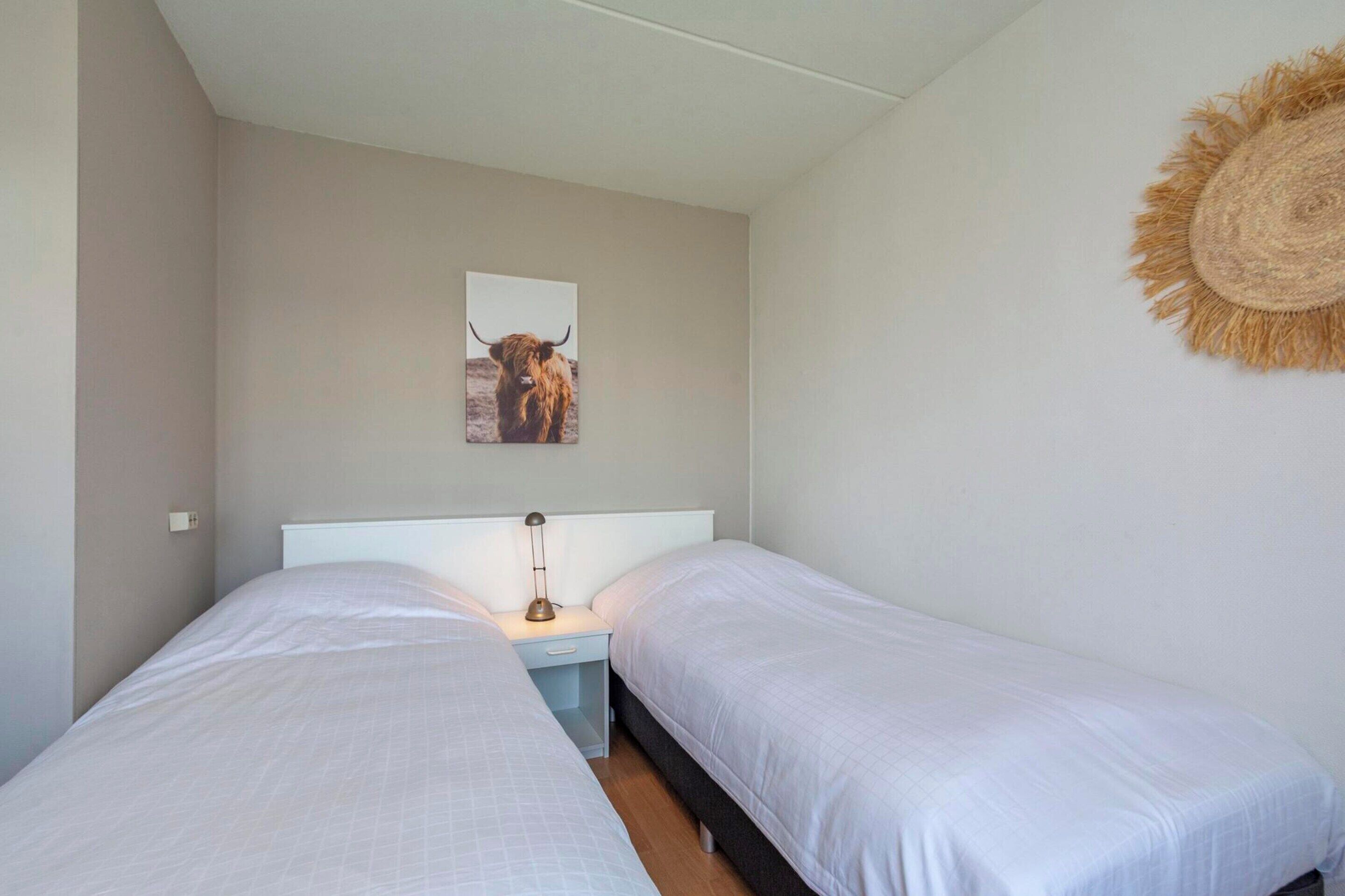 A bedroom with two beds, a nightstand, a lamp, and a wall-mounted artwork of a bull.