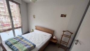Ein Schlafzimmer mit einem hölzernen Bett, einem Fenster mit Vorhängen, einem Nachttisch und einem Holzstuhl.