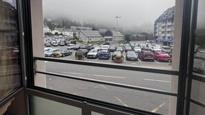 Blick aus einem Fenster auf einen Parkplatz mit mehreren Autos, ein Gebäude mit gewölbtem Dach und einer nebligen Atmosphäre.