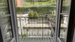 A balcony with a wrought iron railing, a wooden deck, and a view of a garden with a hedge and a small tree. - Apartment in Cauterets, near cable cars, 4 ppl, balcony with mountain view (Cauterets)