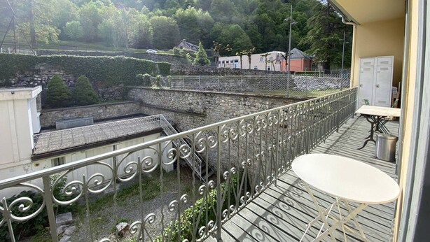 A balcony with a metal railing, a small table, and a view of a mountainous landscape with buildings in the background. - Apartment in Cauterets, near cable cars, 4 ppl, balcony with mountain view (Cauterets)