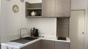 A modern kitchen with a white countertop, two sinks, and wooden cabinetry. There are decorative plates on the wall and a small shelf with a teapot and cups. - Apartment in Cauterets, near cable cars, 4 ppl, balcony with mountain view (Cauterets)