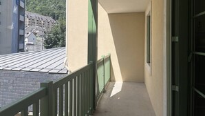 A narrow balcony with a green railing, a concrete floor, and a view of a mountain and buildings in the background. - Cozy apartment in Cauterets with terrace and ski storage (Cauterets)