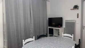 A room with a round table, two chairs, a television on a stand, a radiator, and a curtain. - Cozy apartment in Cauterets with terrace and ski storage (Cauterets)