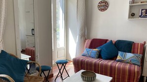 A cozy living room with a striped sofa, a wicker chair, a small table, and a window with curtains. - Studio in Cauterets for 4, ideally located (Cauterets)
