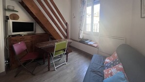 A compact living space with a wooden staircase, a dining area with a TV, a sofa, and a window with a view.
