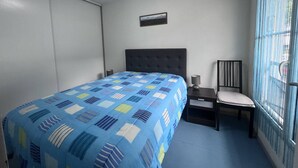 A bedroom with a bed, a chair, a nightstand, and a window with curtains.