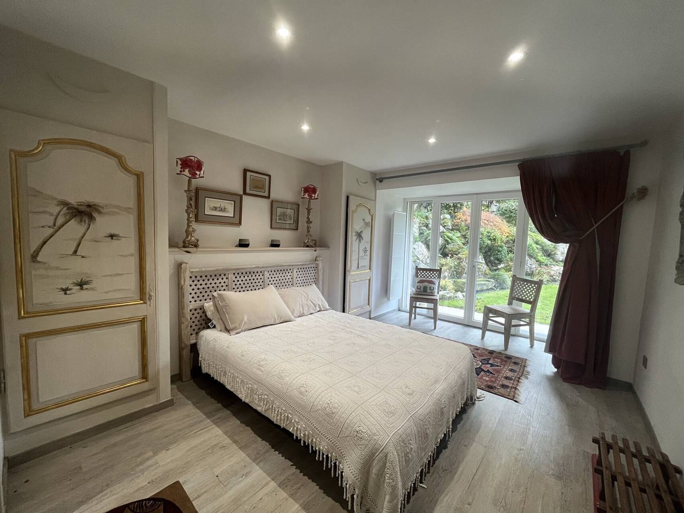 A bedroom with a bed, a large window, and a view of a garden.
