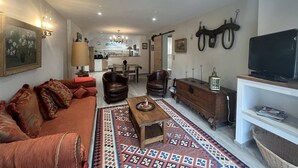 A living room with a sofa, chairs, a coffee table, a TV, and a kitchen in the background.