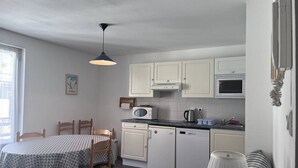 A compact kitchen with white cabinets, a microwave, a kettle, and a coffee machine. There is a dining table with a checkered tablecloth and wooden chairs. - Family apartment in Cauterets with balcony, ski locker, perfect for 4 guests (Cauterets)