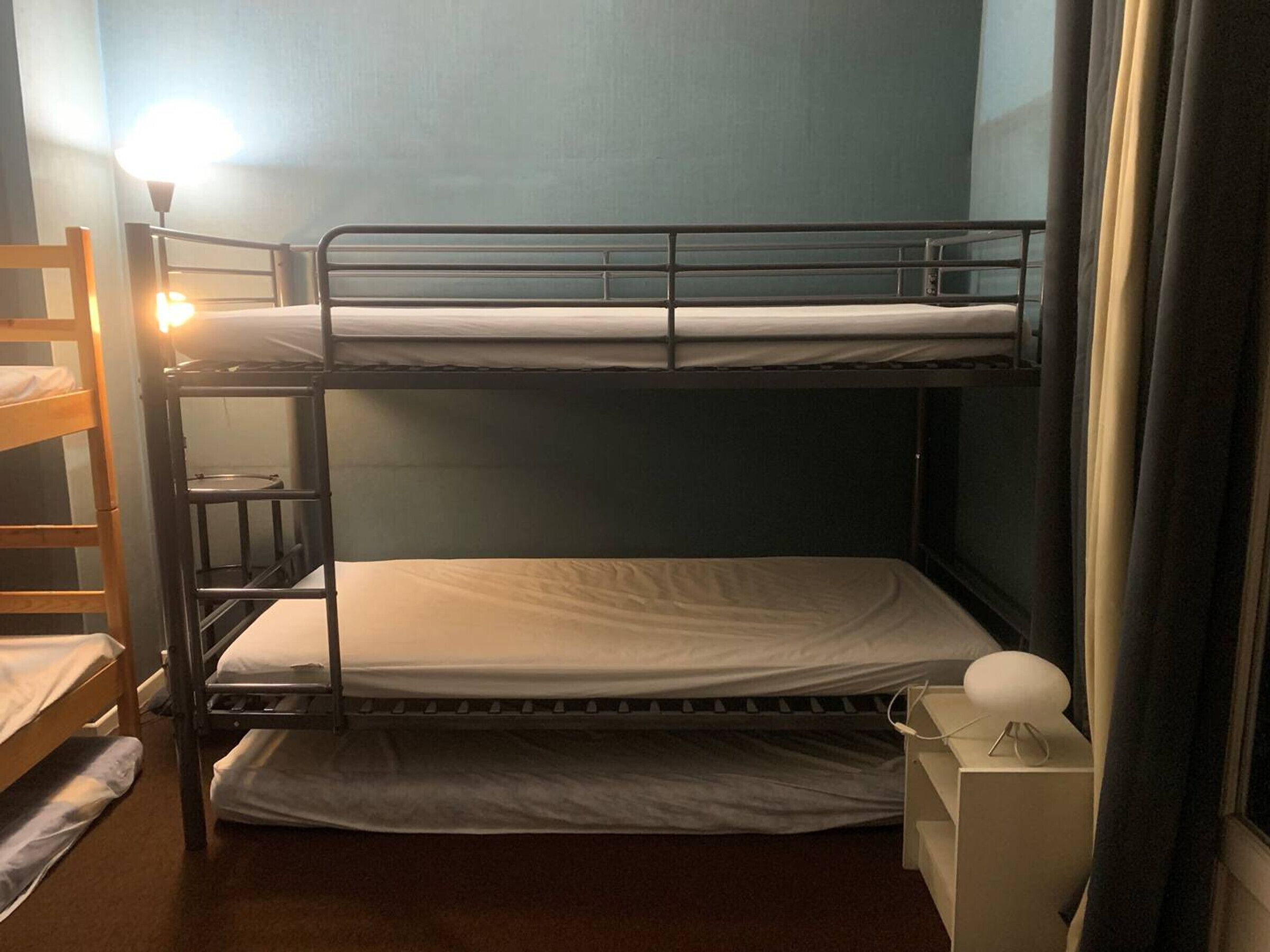 A bunk bed room with a ladder, a bedside table, and a lamp.