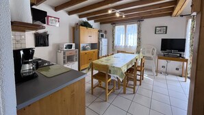 A compact kitchen with a dining area, wooden beams, a microwave, a refrigerator, and a television.