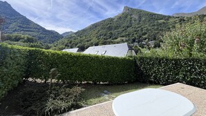 A view of a mountainous landscape with a building in the foreground, surrounded by lush greenery and a clear sky.