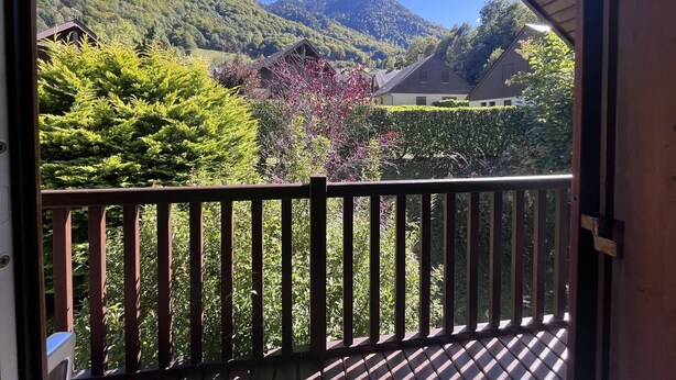 A balcony with a view of a mountainous landscape, a wooden deck, and a clear sky.