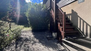 A building with a wooden staircase leading to a porch, a number '99' sign, and a path with trees and shrubs.