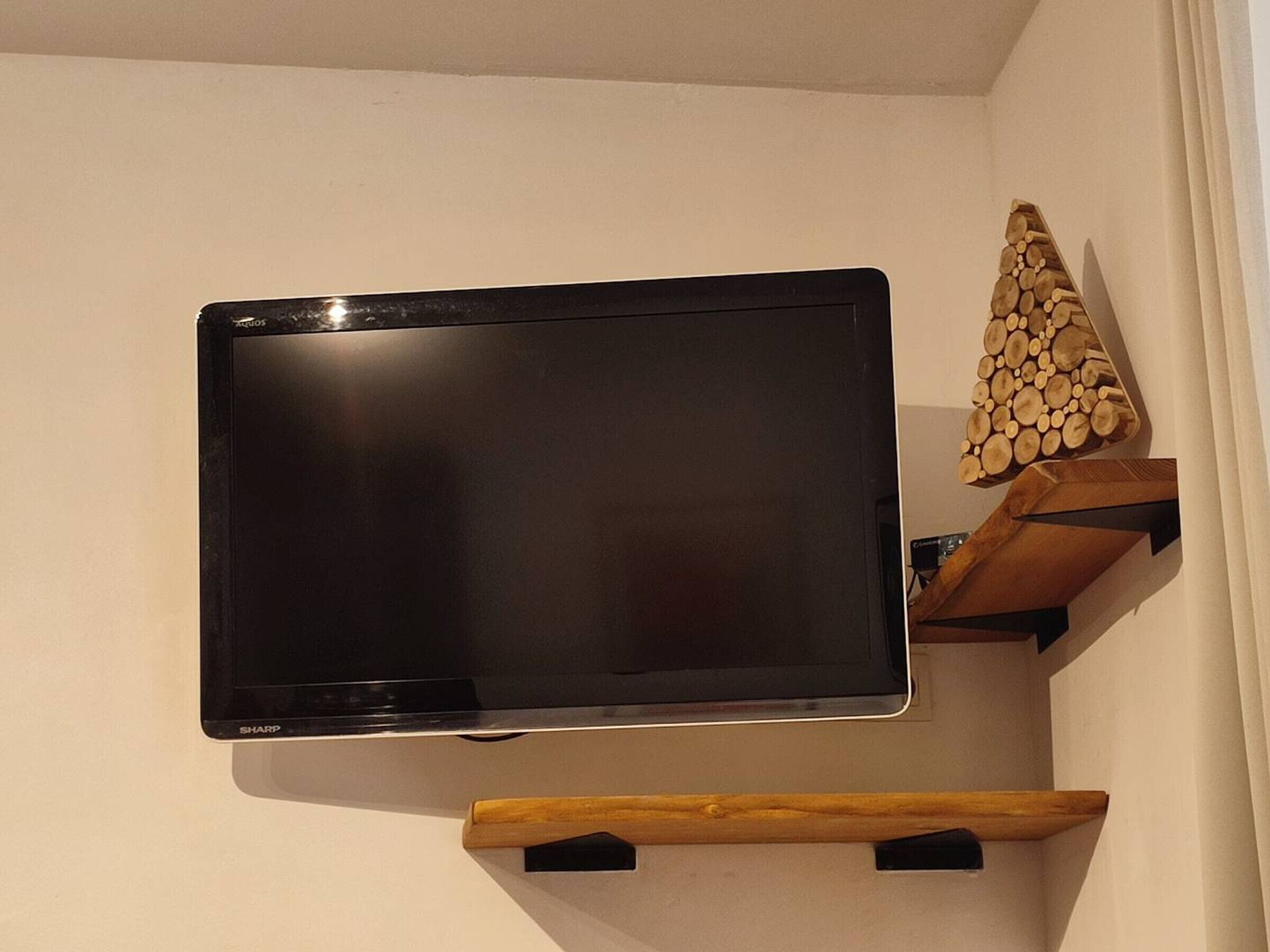 A flat-screen TV mounted on a wall, a wooden shelf with logs, and a small wooden chair.