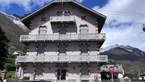 A multi-story building with balconies, a gated entrance, and a mountain backdrop. - Elegant chalet in Cauterets center with terrace (Cauterets)