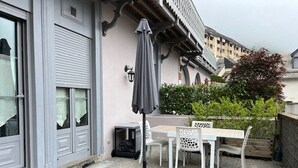 A patio with a table and chairs, a grey umbrella, and a door with a window. - Elegant chalet in Cauterets center with terrace (Cauterets)