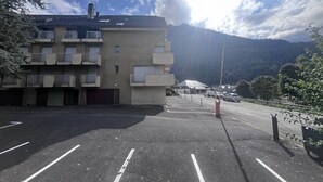 A parking lot with a multi-story building, a mountain in the background, and a clear sky.