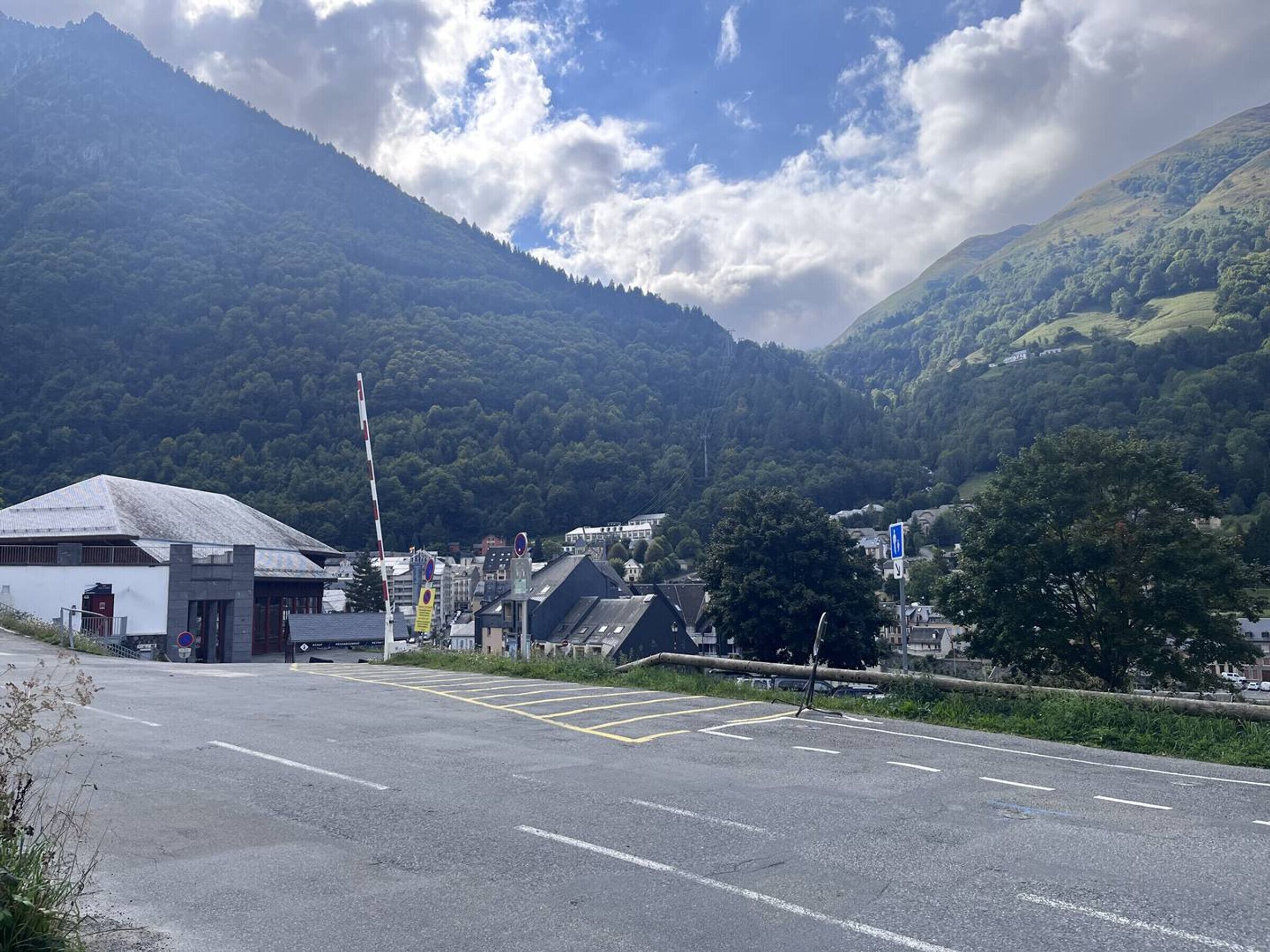 A parking area with a building in the foreground, surrounded by lush green hills and a partly cloudy sky.