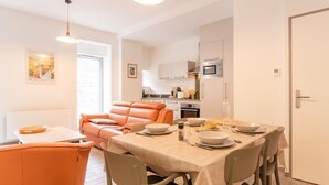 En moderne stue med en sofa, et spisebord dækket til fire personer, og et køkken i baggrunden.