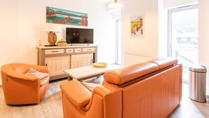 En moderne stue med sofa, lænestol og fjernsyn på et træskab.