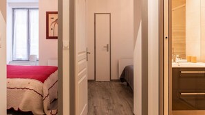 Et hotelværelse med en seng, en dør der fører til et andet værelse, og et badeværelse, der kan ses gennem en åben dør.