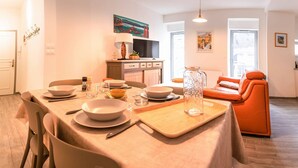 Et moderne spiseområde med et bord dækket til fire personer, et køkken i baggrunden og en lys orange sofa.