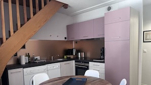 Ett kompakt kök med ett matbord i trä, vita stolar och rosa skåp.