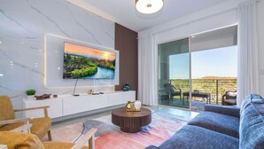 Ein modernes Wohnzimmer mit Fernseher, einer Couch, einem Couchtisch und Blick ins Freie durch große Glastüren.