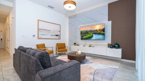 Ein modernes Wohnzimmer mit einem grauen Ecksofa, zwei Sesseln, einem runden Couchtisch, einem flachbildfernseher an der Wand und einer Wand mit Marmor-Musterung.