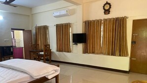 A hotel room with a bed, a television, curtains, a door, and a ceiling fan. - Kappils INN HOMESTAY (Changanassery)