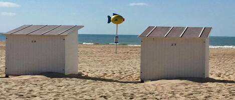 Two beach huts numbered 28 and 27 with a lifeguard tower in the background.