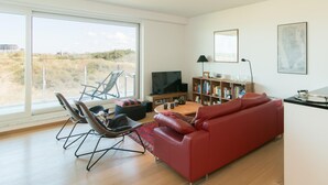 Una sala de estar moderna con un sofá rojo, un televisor, una estantería y un ventanal con vistas al exterior.