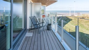 Un balcón con piso de madera, puertas de vidrio y vista al mar.