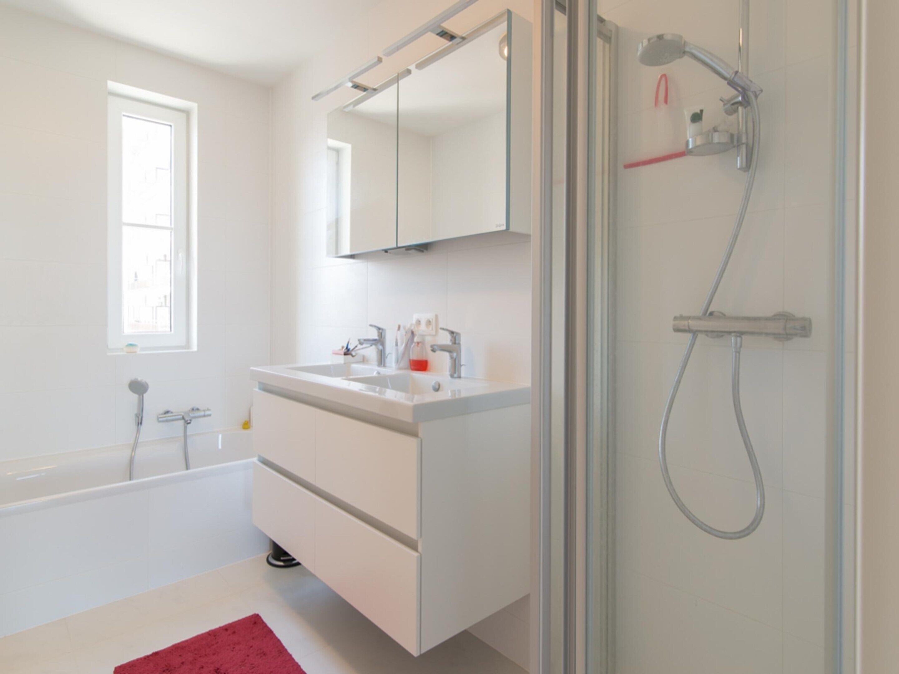 Ein modernes Badezimmer mit einem weißen Waschtisch, einer Duschkabine aus Glas und einer Badewanne.