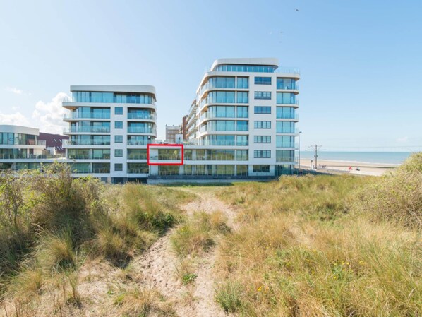 Un bâtiment moderne à plusieurs étages, doté de grandes fenêtres et d’un chemin menant à la plage.