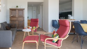 A modern living room with a grey sofa, red and blue chairs, a wooden cabinet, and a dining area with a table and chairs. - Apartment in Ostend With sea Views (Ostend)